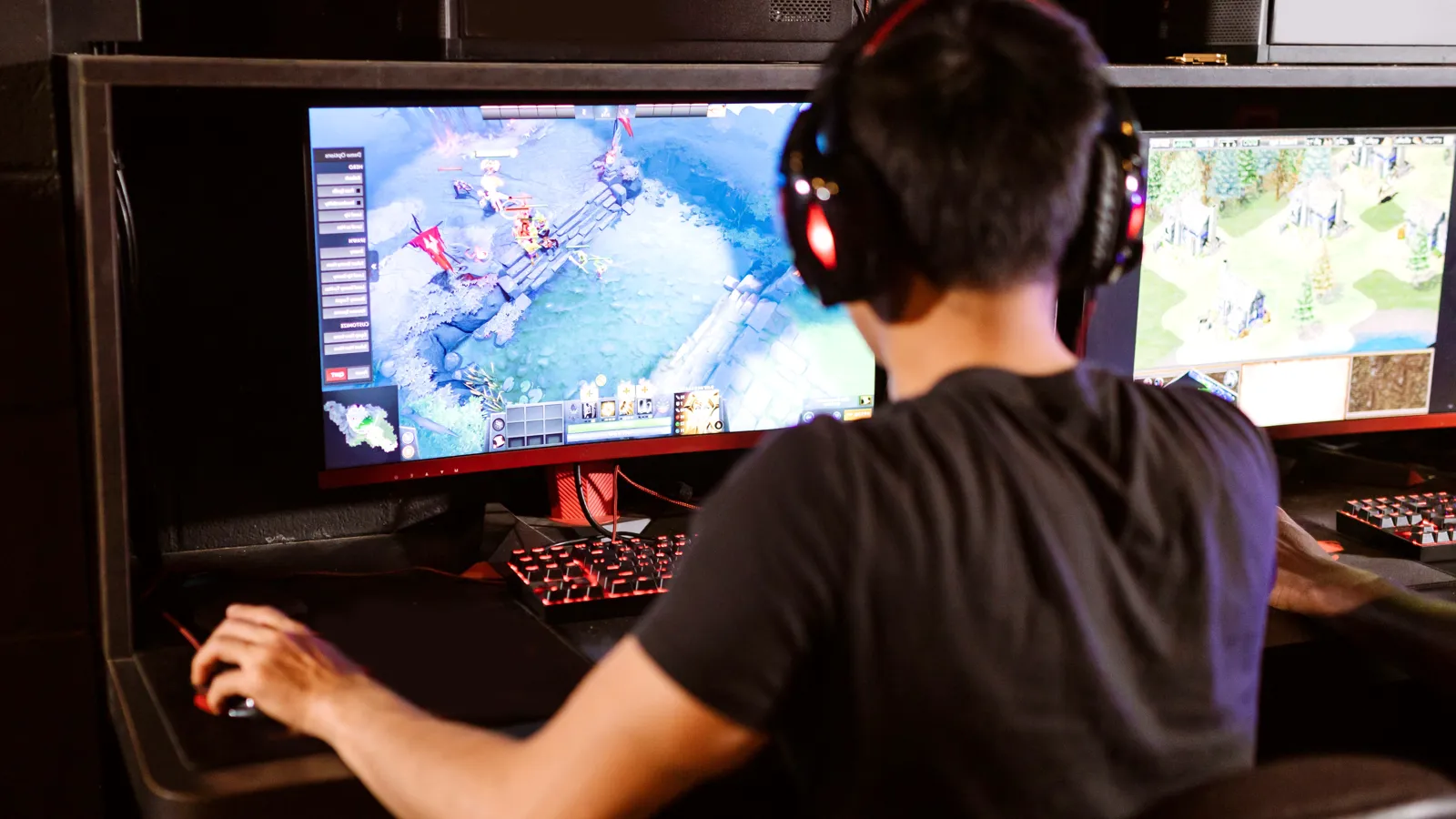 PC gamer in a headset playing at a dual-monitor gaming station